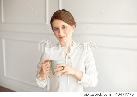 Attractive young woman in casual clothes is holding a cup, looking away and smiling, on white Attractive young woman in casual clothes is holding a cup, looking away and smiling, on white 49477770