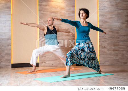 Man and woman with outstretched arms are practicing yoga while standing on blue mat. Man and woman with outstretched arms are practicing yoga while standing on blue mat. 49478069