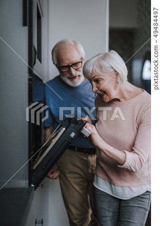 Happy aged couple looking into oven on bakery Happy aged couple looking into oven on bakery 49484497