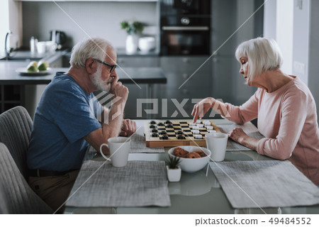 Elder pensioner couple playing checks at home Elder pensioner couple playing checks at home 49484552