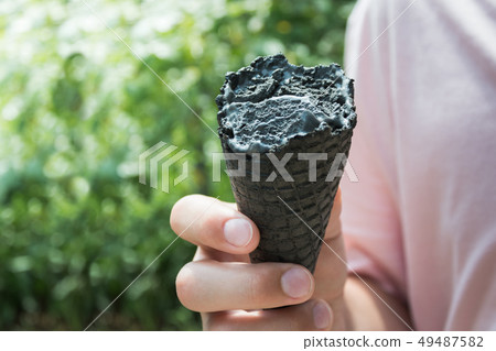 Teen holding in hand bite off black ice cream. 49487582