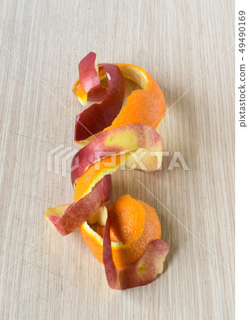 Orange and apple peel intertwined on the table. Orange and apple peel intertwined on the table. 49490169