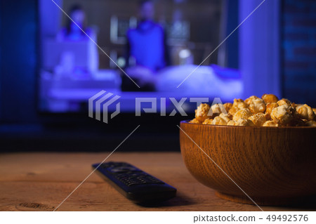 A wooden bowl of popcorn and remote control. 49492576
