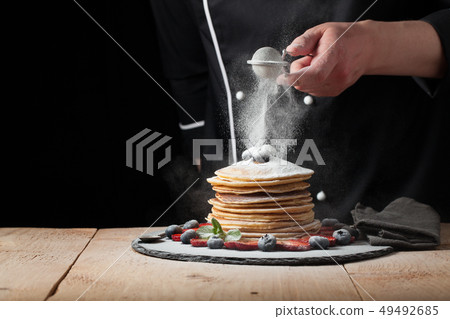 The chef prepares pancakes with berries. 49492685