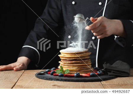 The chef prepares pancakes with berries. 49492687