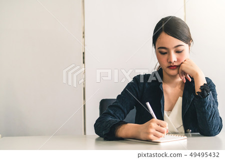 Beautiful young Asian woman writes on notebook. Beautiful young Asian woman writes on notebook. 49495432