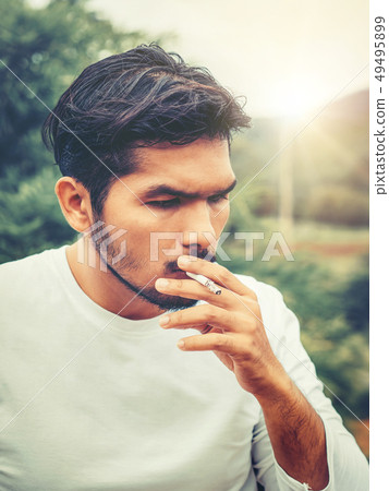 Young man smoking cigarette in the outdoors. 49495899