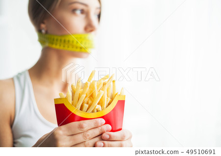 Diet concept and health. Emotional woman with measuring tapes around her mouth and unhealthy foodat 49510691