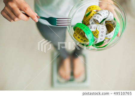 Diet and Weight Loss. Woman holds bowl and fork with measuring tape Diet and Weight Loss. Woman holds bowl and fork with measuring tape 49510765