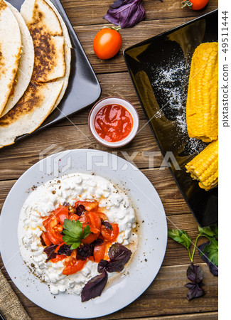 Quesadilla, salad with cottage cheese and tomatoes, two corn on wood table. 49511444