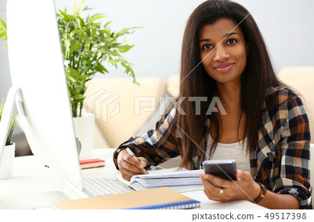 Black smiling woman sitting at workplace writing something Black smiling woman sitting at workplace writing something 49517398