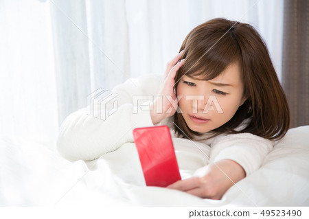Woman looking at smartphone in bed Woman looking at smartphone in bed 49523490