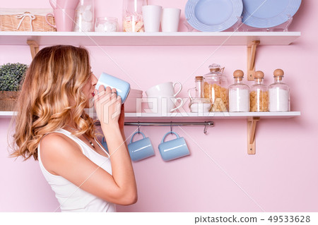 Young happy woman drinking coffee or tea at home in the kitchen. Blonde beautiful girl having her Young happy woman drinking coffee or tea at home in the kitchen. Blonde beautiful girl having her 49533628