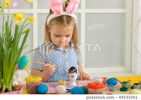 little child girl with Easter bunny ears painting Easter eggs at home. little child girl with Easter bunny ears painting Easter eggs at home. 49535001