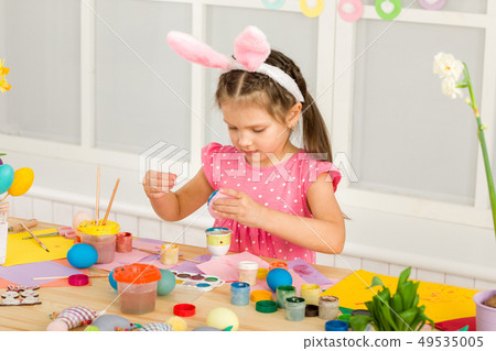 little child girl with Easter bunny ears painting Easter eggs at home. 49535005