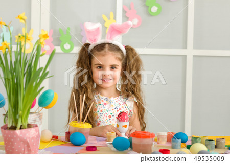 little child girl with Easter bunny ears painting Easter eggs at home. little child girl with Easter bunny ears painting Easter eggs at home. 49535009