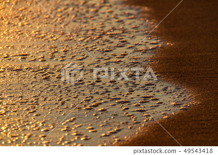 Bubbles of breaking waves on sandy shore at sunset 49543418