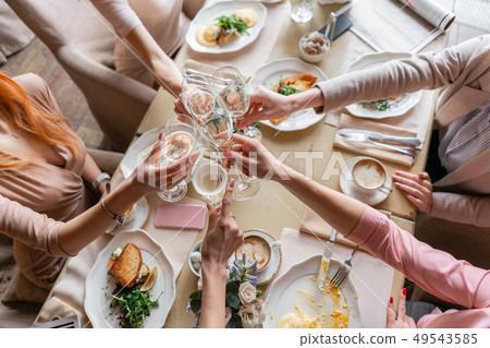 Clink glasses. Five women. Portrait of young people having breakfast at table in restaurant Clink glasses. Five women. Portrait of young people having breakfast at table in restaurant 49543585
