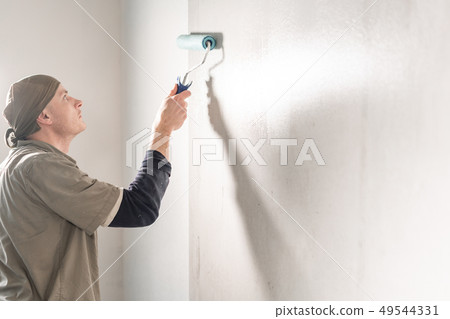 Young man, worker glueing wallpapers on concrete wall. Repair the apartment. Home renovation concept Young man, worker glueing wallpapers on concrete wall. Repair the apartment. Home renovation concept 49544331