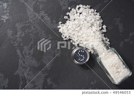 Pile of salt and salt shaker on black stone Pile of salt and salt shaker on black stone 49546055