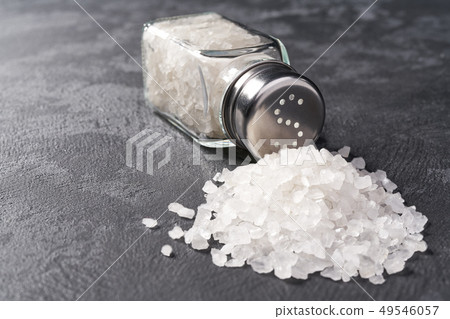 Pile of salt and salt shaker on black stone Pile of salt and salt shaker on black stone 49546057