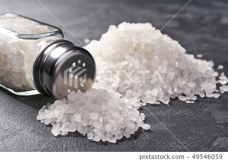 Pile of salt and salt shaker on black stone Pile of salt and salt shaker on black stone 49546059