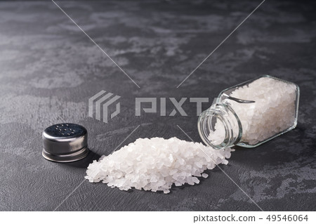 Pile of salt and salt shaker on black stone Pile of salt and salt shaker on black stone 49546064