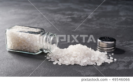 Pile of salt and salt shaker on black stone Pile of salt and salt shaker on black stone 49546066