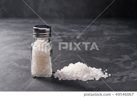 Pile of salt and salt shaker on black stone Pile of salt and salt shaker on black stone 49546067