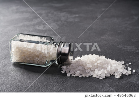 Pile of salt and salt shaker on black stone Pile of salt and salt shaker on black stone 49546068
