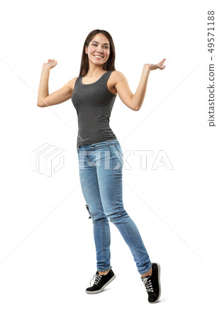 Young smiling woman in sleeveless gray top and blue jeans standing on tiptoes with arms bent and Young smiling woman in sleeveless gray top and blue jeans standing on tiptoes with arms bent and 49571188