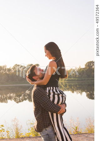 Romantic, people and summer concept - man raised a woman in his arms near the lake at the sunset Romantic, people and summer concept - man raised a woman in his arms near the lake at the sunset 49572364