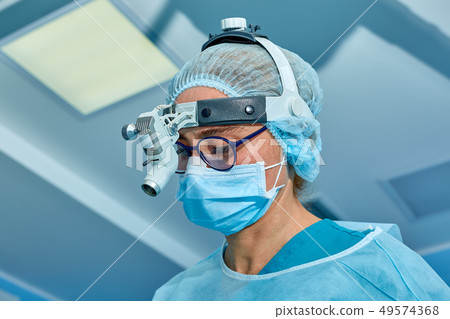 Close up portrait of female surgeon doctor wearing protective mask and hat during the operation 49574368