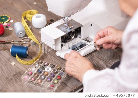 Close-up of senior woman seamstress hands removing the bobbin case in order to do the maintenance of Close-up of senior woman seamstress hands removing the bobbin case in order to do the maintenance of 49575077