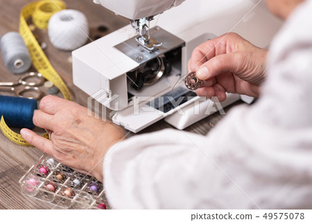 Close-up of senior woman seamstress hands removing the bobbin case in order to do the maintenance of Close-up of senior woman seamstress hands removing the bobbin case in order to do the maintenance of 49575078