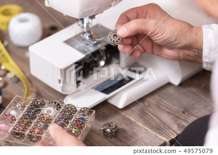 Close-up of senior woman seamstress hands removing the bobbin case in order to do the maintenance of Close-up of senior woman seamstress hands removing the bobbin case in order to do the maintenance of 49575079