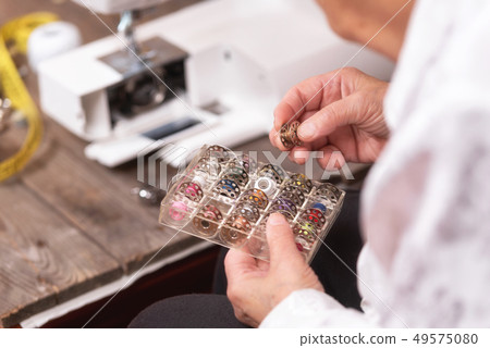 Close up on seamstress hands choosing threads for electrical sewing machine. 49575080