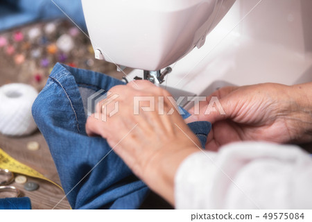 Close-up of senior woman hands seamstress sewing jeans on electrical sewing machine. 49575084
