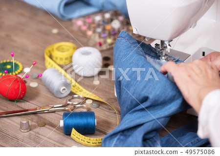 Close-up of senior woman hands seamstress sewing jeans on electrical sewing machine. 49575086