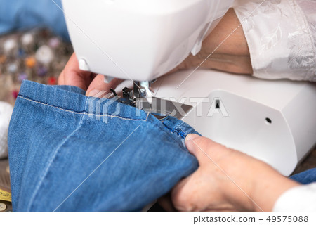 Close-up of senior woman hands seamstress sewing jeans on electrical sewing machine. 49575088