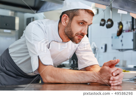 We know our food. Male chef leaning on the table and looking aside while going to cook We know our food. Male chef leaning on the table and looking aside while going to cook 49586298