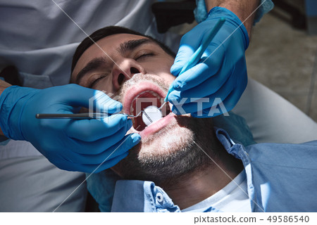 Bringing life to your smile. Dentist in latex gloves examining male patient, lying in dental chair 49586540