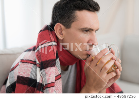 Man with Cold Sitting on Sofa in Checkered Blanket Man with Cold Sitting on Sofa in Checkered Blanket 49587256