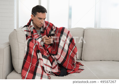 Man with Cold Sitting on Sofa in Checkered Blanket 49587267