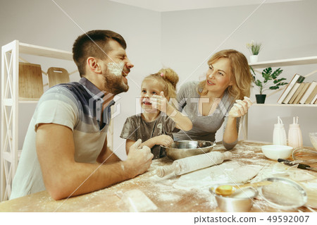 Cute little girl and her beautiful parents preparing the dough for the cake in kitchen at home 49592007