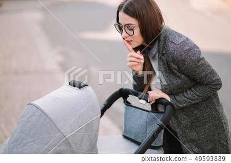 Young mother walking with her baby in stroller and putting finger up to lips and saying shh. Mom Young mother walking with her baby in stroller and putting finger up to lips and saying shh. Mom 49593889
