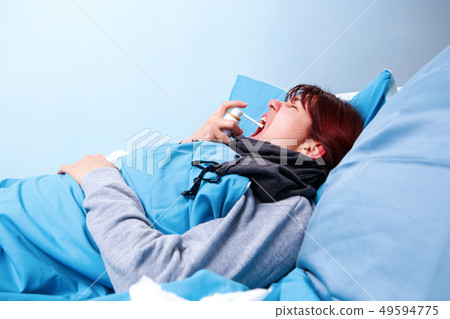 Image of sick brunette using throat spray lying in bed . Image of sick brunette using throat spray lying in bed . 49594775