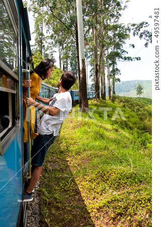 Couple hanging outside of train in Sri Lanka Couple hanging outside of train in Sri Lanka 49597481