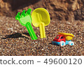 Children's toy truck with gravel or sand. Yellow scoop and green rake on the background. Concept of 49600120