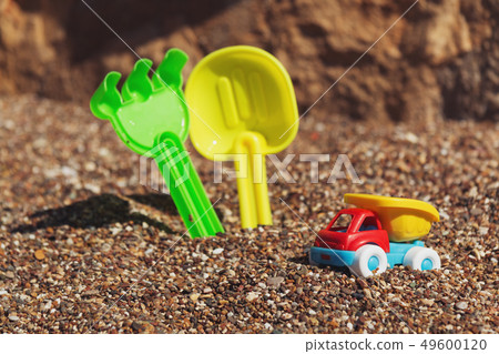 Children's toy truck with gravel or sand. Yellow scoop and green rake on the background. Concept of Children's toy truck with gravel or sand. Yellow scoop and green rake on the background. Concept of 49600120